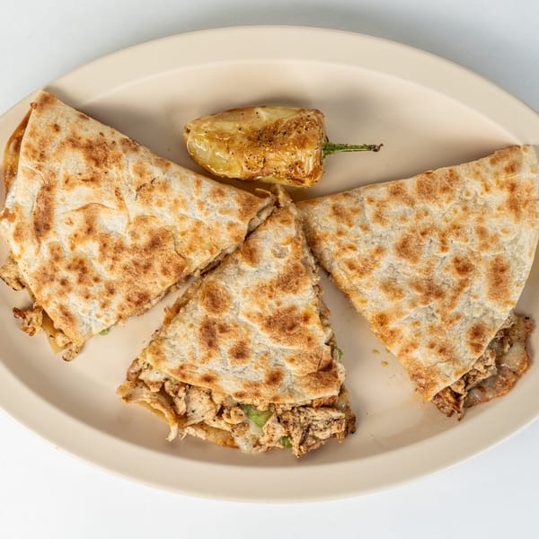 Three chicken quesadilla slices and a roasted green pepper on a light-colored oval plate.