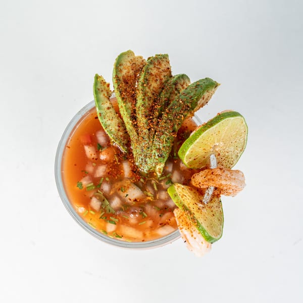 Overhead view of a Mexican shrimp cocktail with avocado, lime, and chili powder.