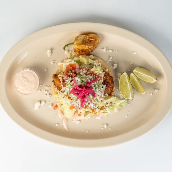 Mexican tostada with chicken, lettuce, cheese, red onions, and lime wedges on a beige plate.