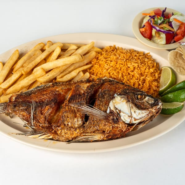 Fried whole fish with rice, french fries, lime wedges, tortillas, and a side salad.